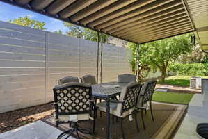 Covered patio featuring an adjustable louvered awning, concrete flooring, and a privacy fence