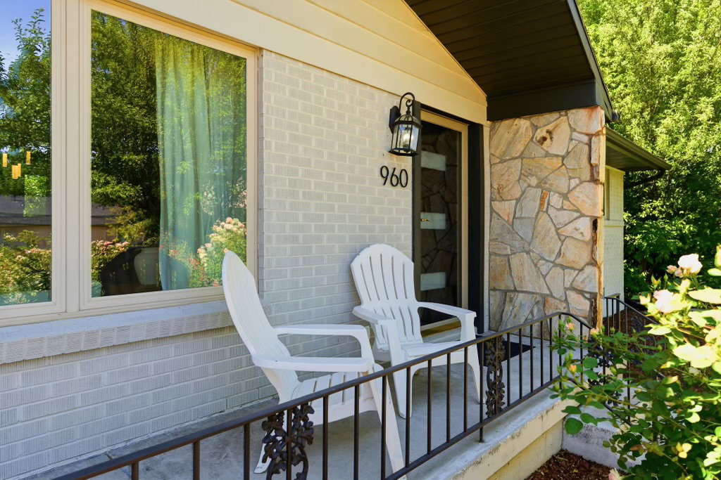 Front entry featuring a stone facade, painted brick exterior, dark-framed door with numerical address, and a black wrought iron railing