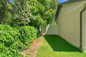 Side yard featuring a white privacy fence, mature green foliage, and a raised garden bed with wood borders