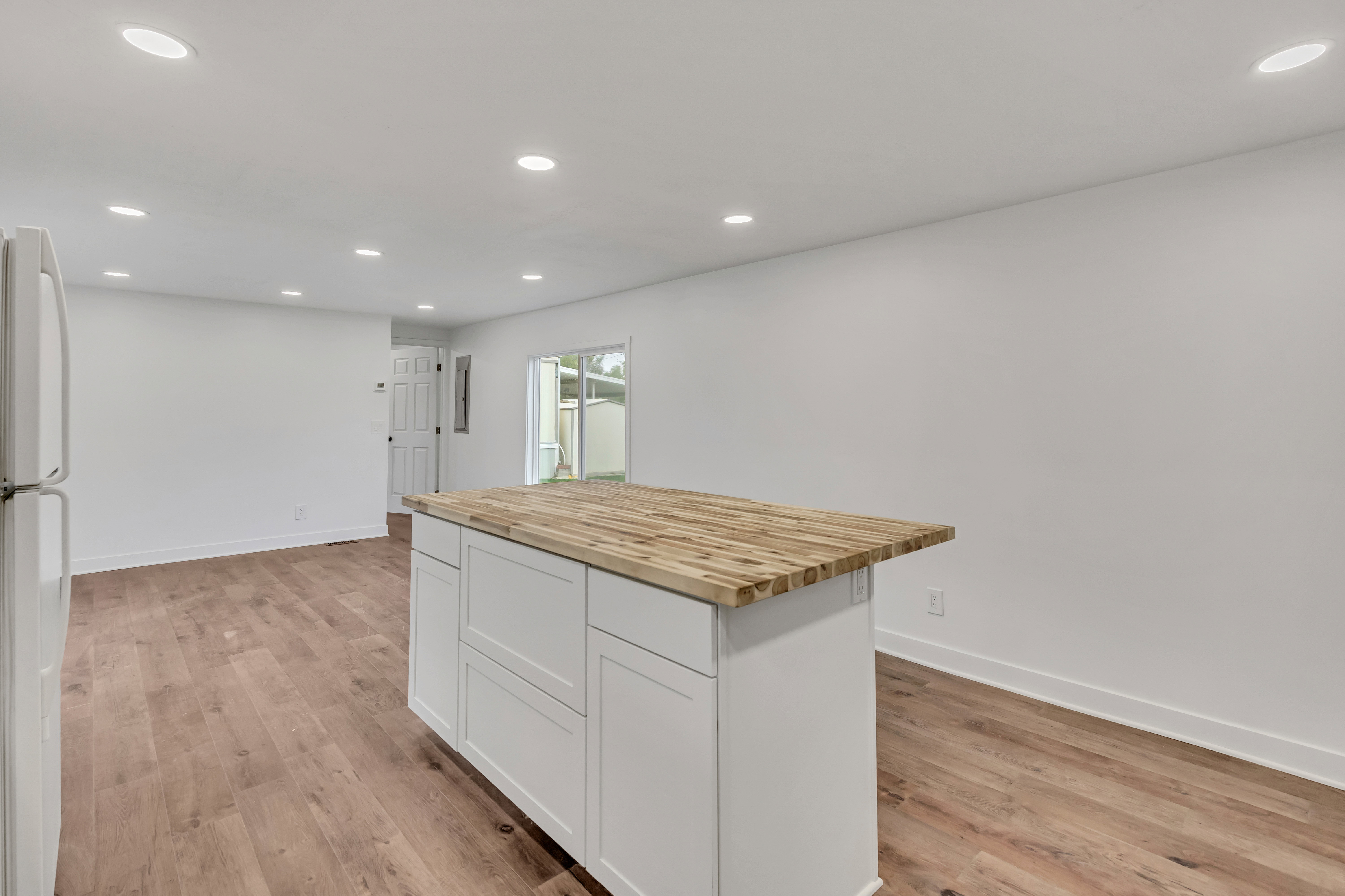 Kitchen with butcher block counters, recessed lighting, freestanding refrigerator, white cabinetry, and a kitchen island