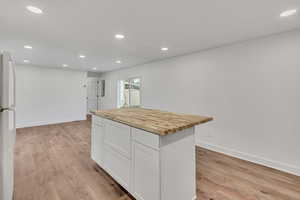Kitchen with butcher block counters, recessed lighting, freestanding refrigerator, white cabinetry, and a kitchen island