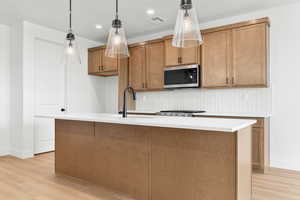 Kitchen featuring wood finish cabinetry, a kitchen island with sink, decorative light fixtures, light wood-style floors, and stainless steel microwave
