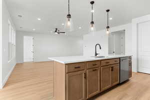 Kitchen with decorative light fixtures, a center island with sink, ceiling fan, and light wood finished floors