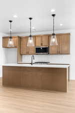 Kitchen featuring wood finish cabinets, pendant lighting, an island with sink, and light wood finished floors