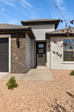 View of exterior entry featuring stucco siding, stone siding, a garage, concrete driveway, and a tiled roof