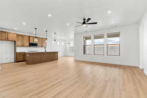 Kitchen featuring open floor plan, wood finish cabinets, a center island with sink, light countertops, and ceiling fan