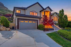Twilight view of the home featuring stone siding, stucco siding, concrete driveway, and an attached garage