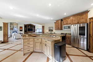 Kitchen featuring stainless steel appliances, inlaid floor details, open floor plan, a fireplace, and a kitchen island