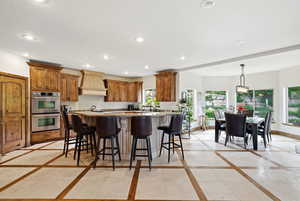 Kitchen with inlaid floor details, a breakfast bar, light stone counters, stainless steel double oven, and wood finish cabinets