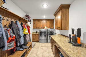 Laundry area featuring cabinet space, a textured ceiling, light tile patterned floors, and washing machine and clothes dryer
