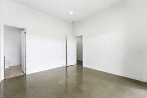 Unfurnished bedroom featuring finished concrete floors, connected bathroom, and a high ceiling