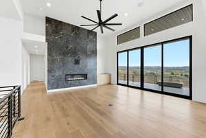 Unfurnished living room with ceiling fan, a tiled fireplace, a high ceiling, light wood-type flooring, and a mountain view