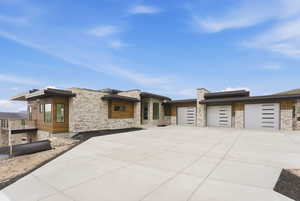 View of front of house with an attached garage, concrete driveway, and stone siding