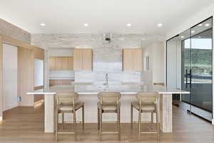 Kitchen with light wood finish cabinets, light stone countertops, a kitchen bar, light wood-type flooring, and recessed lighting
