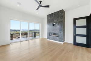 Unfurnished living room with a ceiling fan, a mountain view, a large fireplace, and light wood-style floors