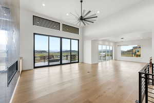 Unfurnished living room with a mountain view, a glass covered fireplace, light wood finished floors, a high ceiling, and recessed lighting