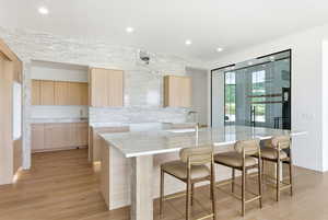 Kitchen featuring light wood finish cabinets, light stone counters, light wood-type flooring, a breakfast bar, and a kitchen island with sink