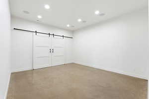 Unfurnished bedroom with a barn door, recessed lighting, and concrete floors