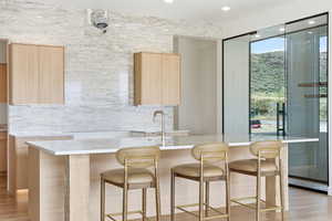 Kitchen featuring light wood finish cabinetry, light stone countertops, an island with sink, modern cabinets, and light wood-style flooring