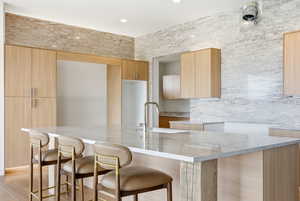 Kitchen with light wood finish cabinets, light stone counters, modern cabinets, a breakfast bar area, and recessed lighting