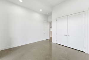 Unfurnished bedroom featuring finished concrete floors, a closet, and recessed lighting