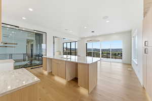 Kitchen with light wood finish cabinets, modern cabinets, light stone counters, a large island, and light wood-type flooring