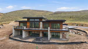 Rear view of house featuring a patio, stone siding, a balcony, and a mountain view