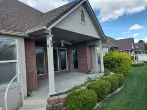 Rear view of property with brick siding, a ceiling fan, roof with shingles, and stucco siding