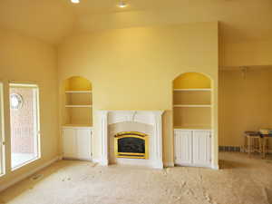 Unfurnished living room with built in features, carpet, a tiled fireplace, and vaulted ceiling