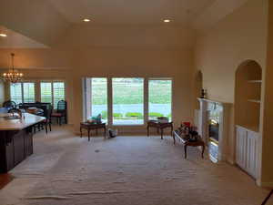 Living room with light colored carpet, a high end fireplace, a chandelier, plenty of natural light, and vaulted ceiling