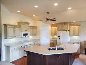Kitchen with white appliances, a kitchen bar, a ceiling fan, a large island with sink, and recessed lighting