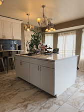 Kitchen featuring light marble finish floors, white cabinetry, a center island, suspended lighting, and a textured ceiling