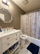 Full bath with vanity, shower / tub combo, a textured ceiling, and light marble finish floors