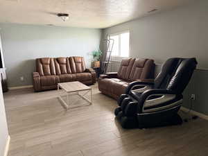Living room with a textured ceiling, light wood-style floors, and a wainscoted wall