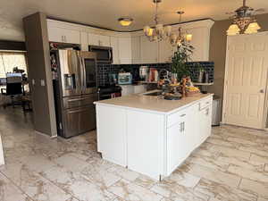 Kitchen featuring white cabinets, stainless steel appliances, tasteful backsplash, a center island, and a chandelier