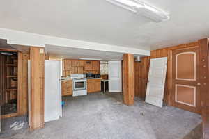 Kitchen with white appliances, carpet, wooden walls, light countertops, and wood finish cabinetry