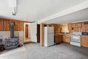 Kitchen with wooden walls, white appliances, a wood stove, light colored carpet, and wood finish cabinets