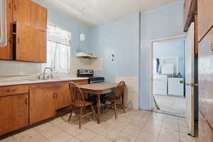 Kitchen with wood finish cabinetry, light countertops, electric range, washer and dryer, and hanging light fixtures