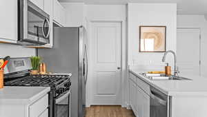 Kitchen with stainless steel appliances, a peninsula, light countertops, white cabinets, and light wood finished floors