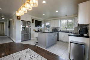 Kitchen with dark countertops, stainless steel fridge with ice dispenser, white cabinetry, light tile patterned floors, and a kitchen breakfast bar.