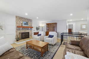 Living area with a stone fireplace, light wood-style floors, and recessed lighting