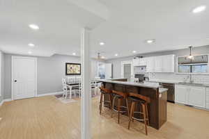 Dual tone kitchen with granite countertops, a kitchen bar, two tone cabinetry, a center island, and light wood-style flooring