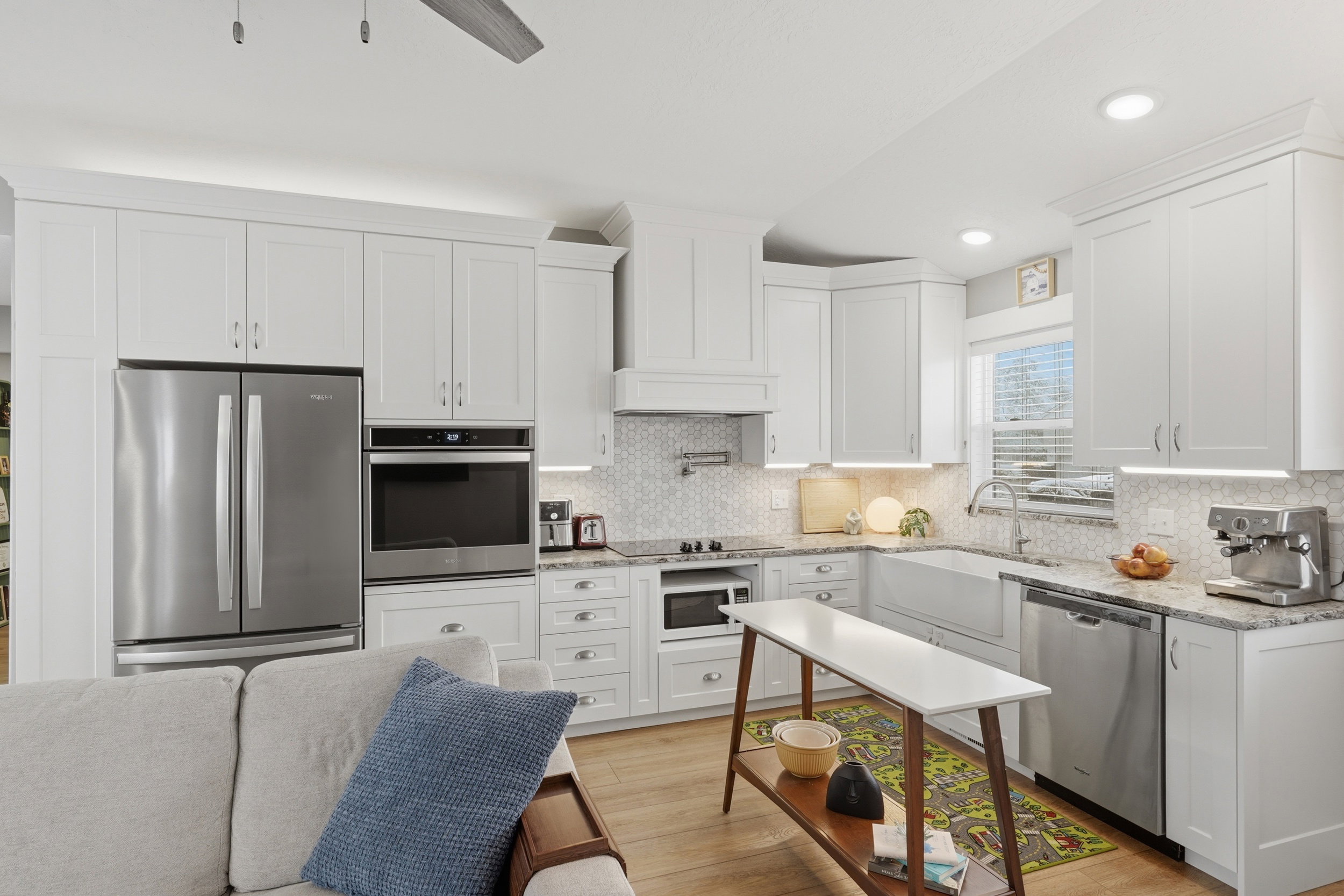 ADU Kitchen with stainless steel appliances, farmhouse sink,  white cabinets, Granite counters, light wood finished floors, and recessed lighting