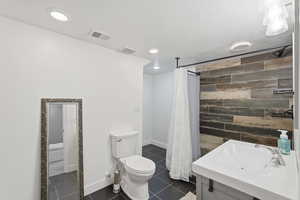 ADU lower level Bathroom featuring wooden walls, vanity, a stall shower, dark tile patterned flooring, and a textured ceiling