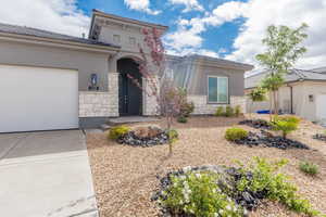 View of front facade with stone siding, stucco siding, a garage, and concrete driveway