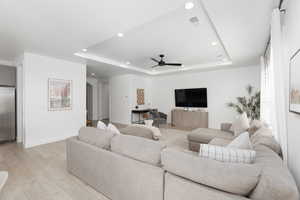 Living area with arched walkways, light wood finished floors, a tray ceiling, a ceiling fan, and recessed lighting