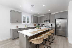 Kitchen featuring gray cabinets, stainless steel appliances, a breakfast bar, recessed lighting, and light wood finished floors