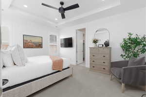 Bedroom with a raised ceiling, recessed lighting, light carpet, ensuite bathroom, and ceiling fan