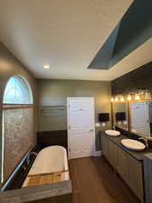 Full bath with a bath, double vanity, dark wood-style floors, and a textured ceiling