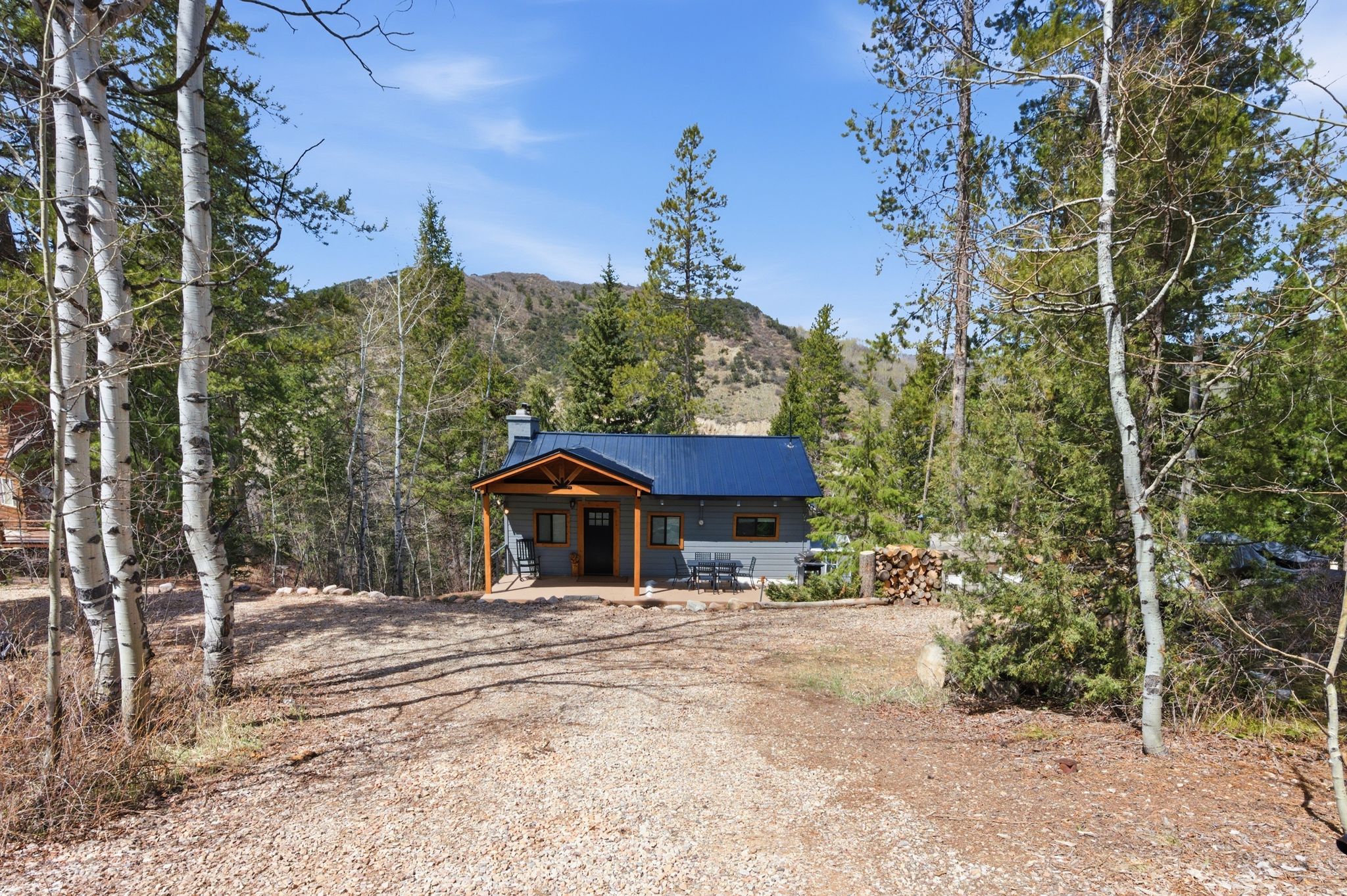 View of front of home with a patio area, a mountain view, a metal roof, graveled horseshoe shaped driveway, and a chimney